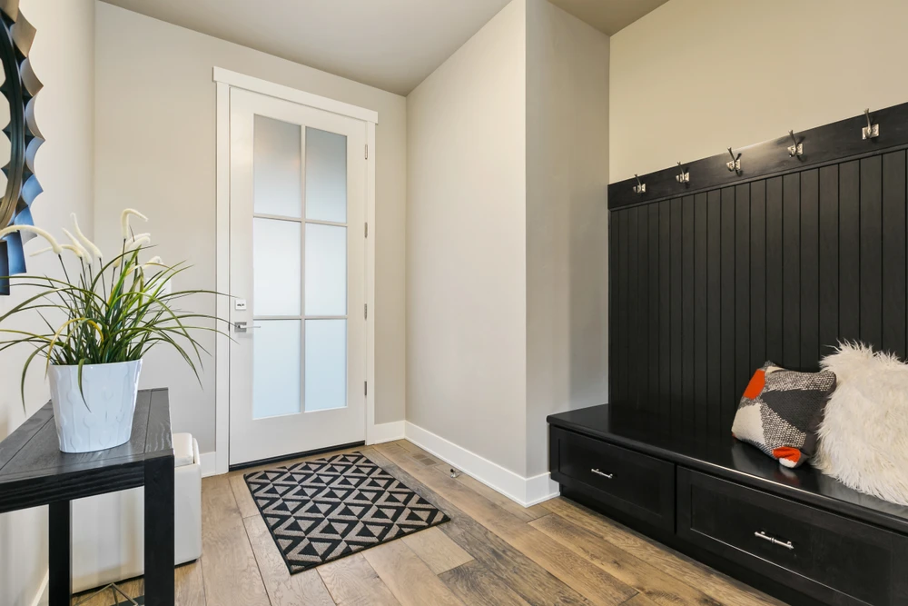 Entr&eacute;e r&eacute;sidentielle moderne avec banc de rangement int&eacute;gr&eacute; en bois noir, crochets muraux et coussins d&eacute;coratifs