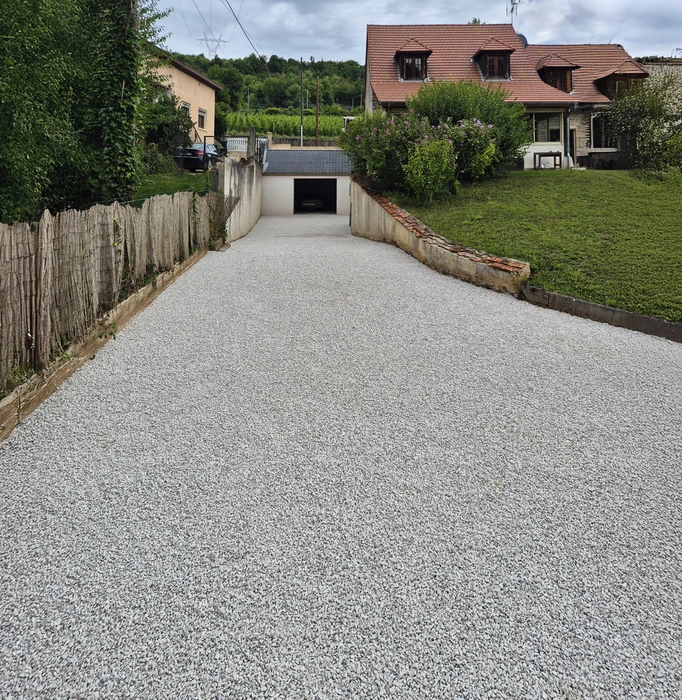 Allée résidentielle en pente descendante menant à un garage souterrain, bordée de maisons individuelles avec toitures en tuiles rouges et jardins paysagers