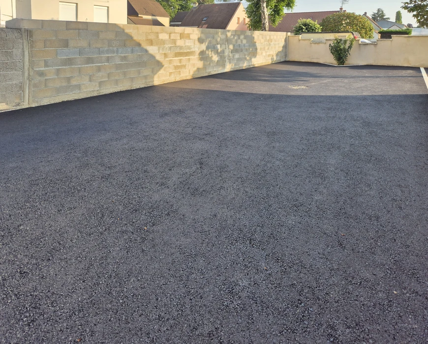 Extérieur résidentiel, allée goudronnée fraîchement revêtue devant maison en pierre naturelle beige