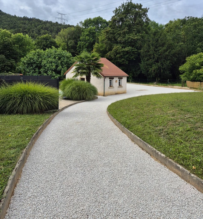 Extérieur résidentiel, allée goudronnée fraîchement revêtue devant maison en pierre naturelle beige