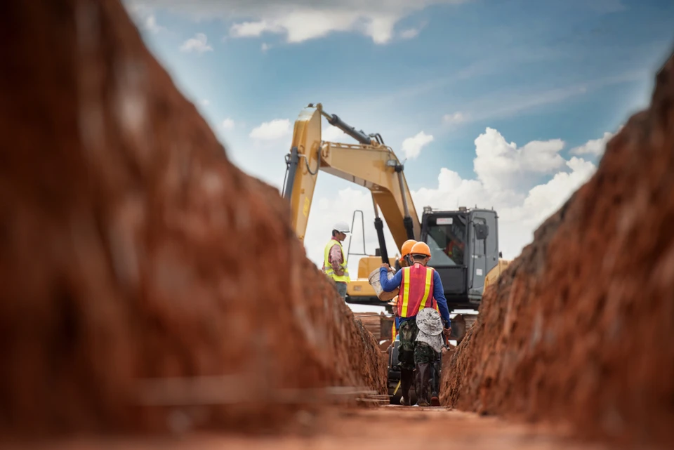 Chantier de travaux publics en extérieur avec pelleteuse sur chenilles effectuant des opérations de terrassement près d'un cours d'eau