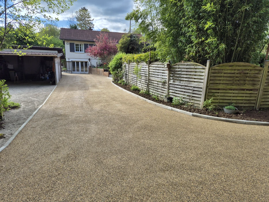 Allée de gravier en cours d'aménagement dans un jardin résidentiel, bordée d'arbres et végétation dense