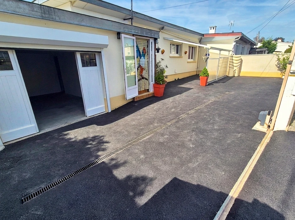 Extérieur résidentiel, allée goudronnée fraîchement revêtue devant maison en pierre naturelle beige
